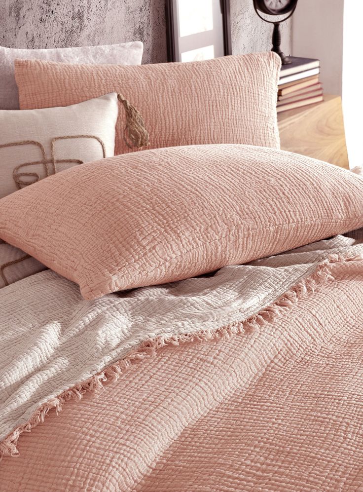 an unmade bed with several pillows and blankets on top of it in front of a clock