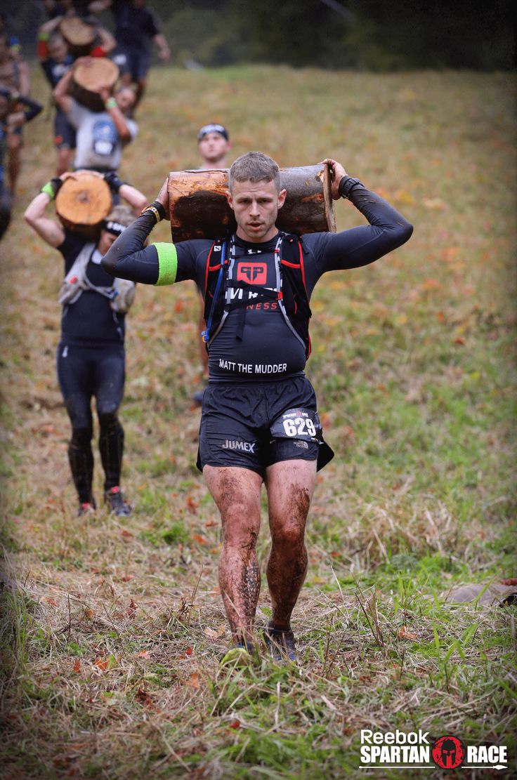 the men are carrying their logs across the field to finish the race in the woods