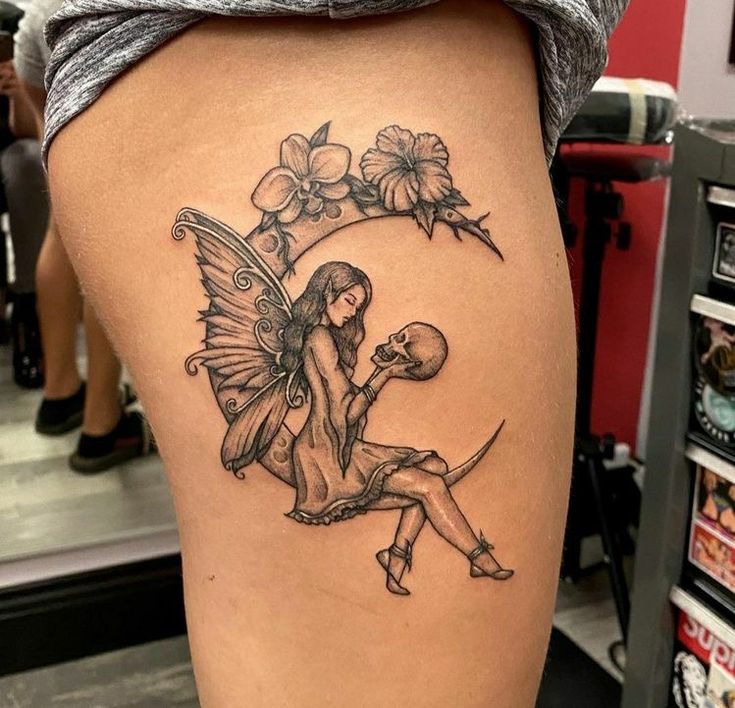 a woman's thigh with a fairy sitting on the moon and flowers around her