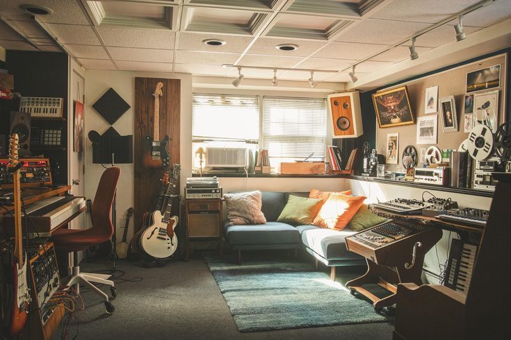 a living room filled with lots of musical equipment and guitars on the wall next to a couch