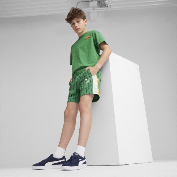 a young boy is leaning against a wall wearing shorts and a green t - shirt