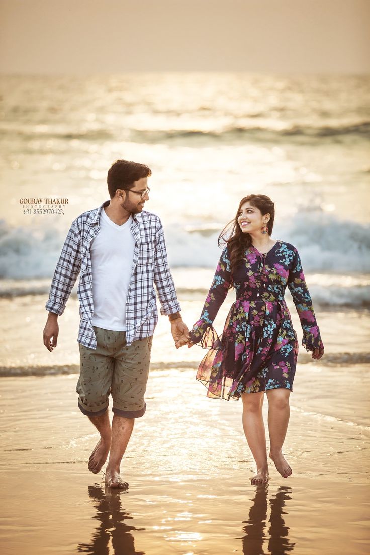 a man and woman holding hands while walking on the beach at sunset with waves coming in