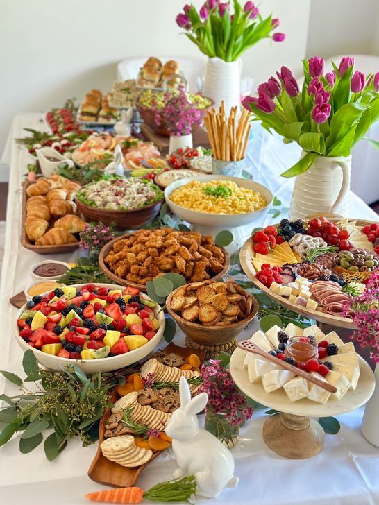 a table topped with lots of different types of foods and desserts next to vases filled with flowers