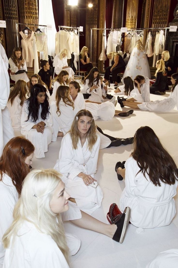 a group of women sitting on the ground in front of white dresses and high heels