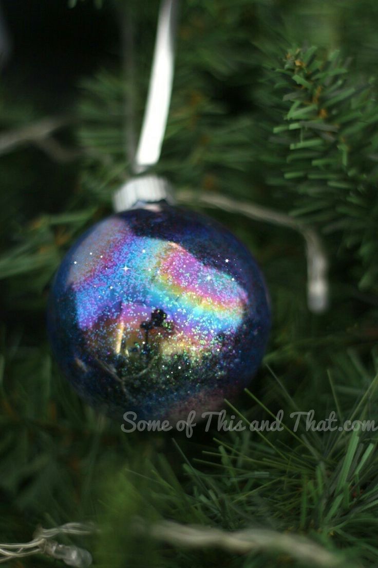 a glass ornament hanging on a christmas tree with a rainbow in the sky