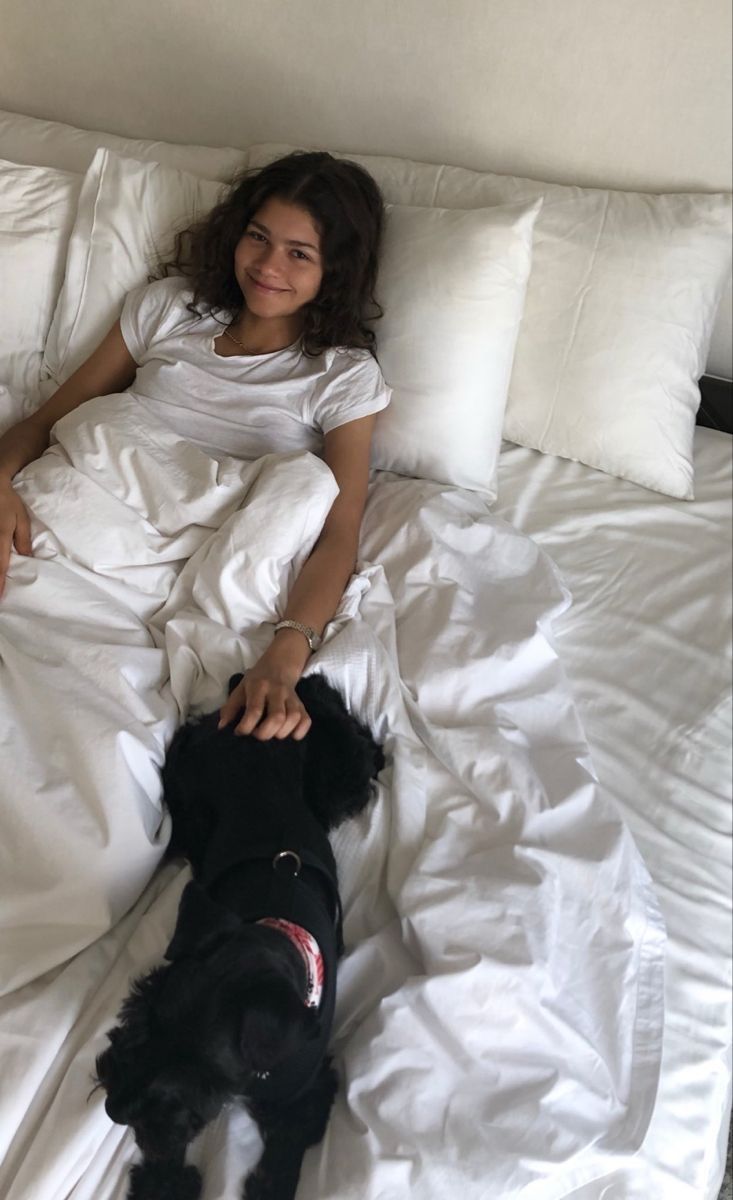 a woman laying in bed next to a black dog on top of a white sheet