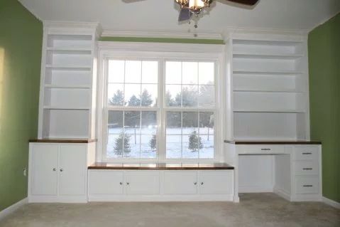 an empty living room with green walls and white built - in shelving units, including a ceiling fan