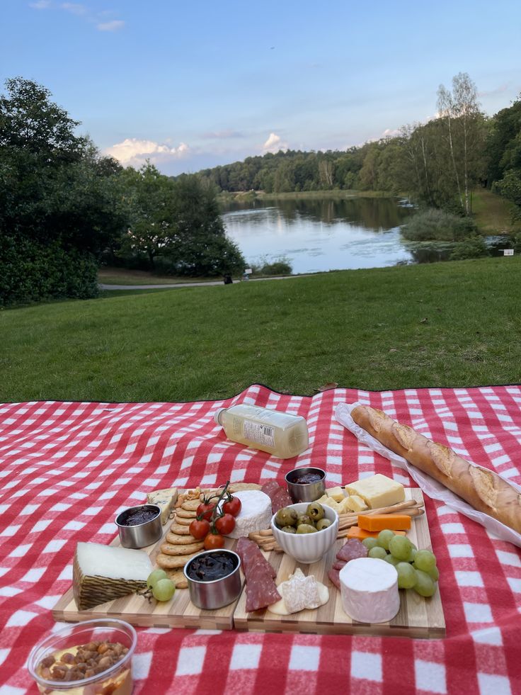 a picnic table with cheese, crackers and fruit on it in front of a lake