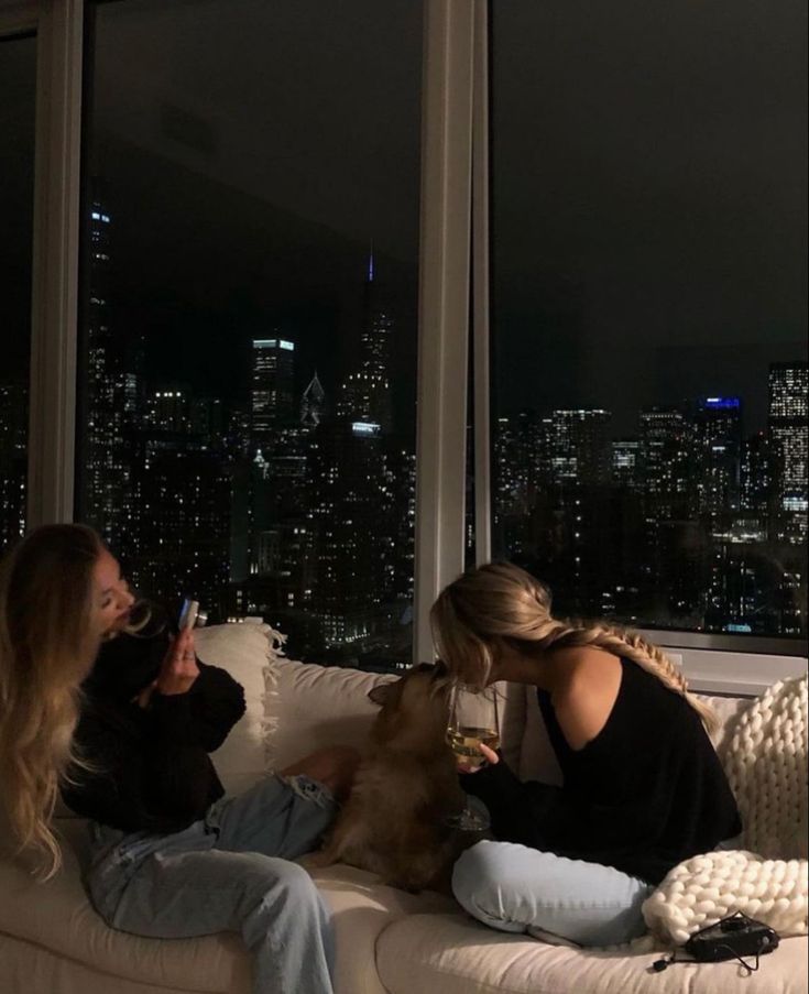 two women sitting on a couch with a dog in their lap looking out the window