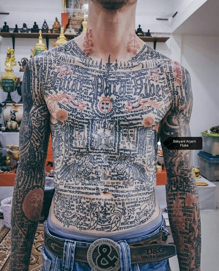 a man with tattoos on his body and chest standing in a room full of shelves