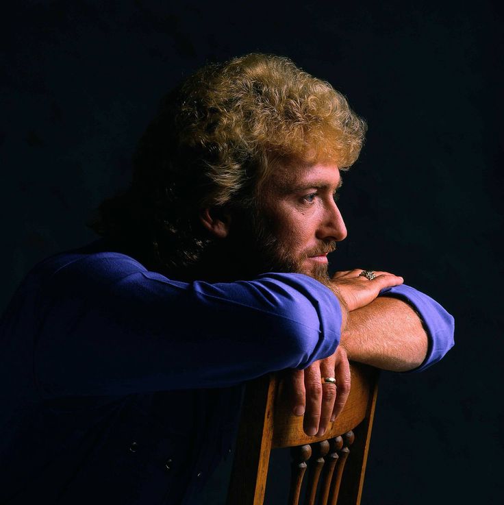 a man sitting on top of a wooden chair with his arms resting on the back