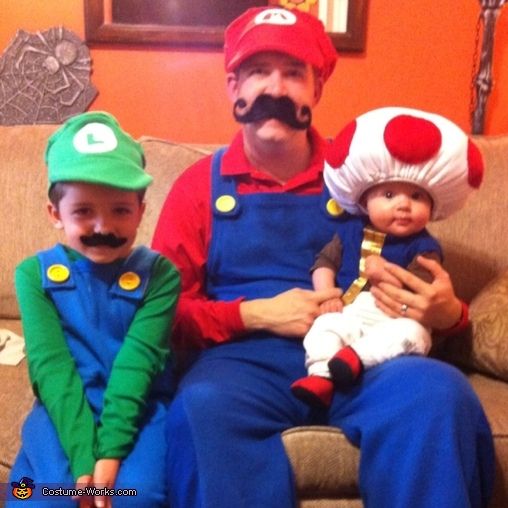 three people dressed up as mario and luigi with their baby on his lap, sitting next to each other