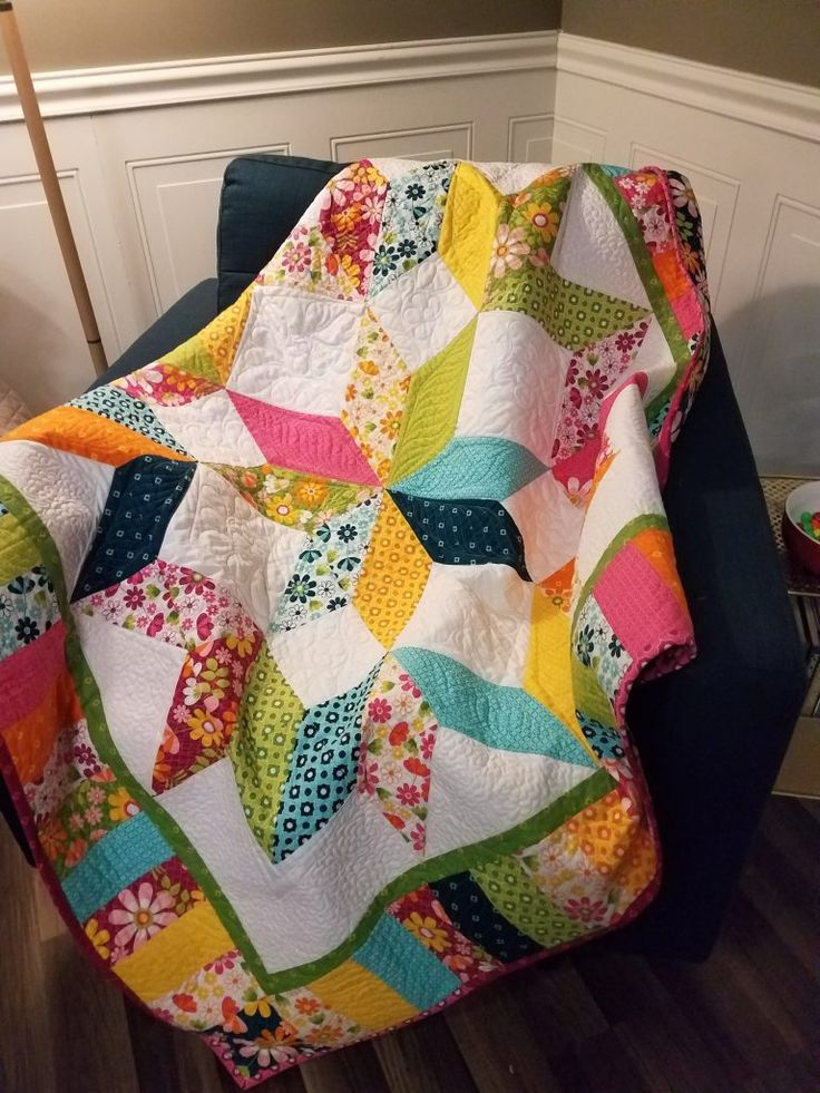 a colorful quilt sitting on top of a blue chair next to a wall with white trim