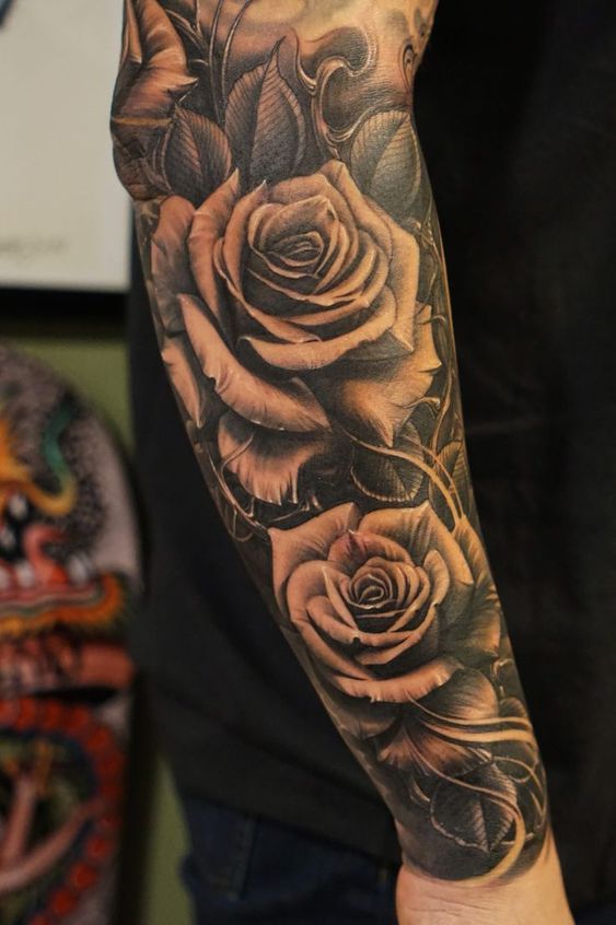 a man's arm with roses and leaves tattooed on the forearm, in black and grey