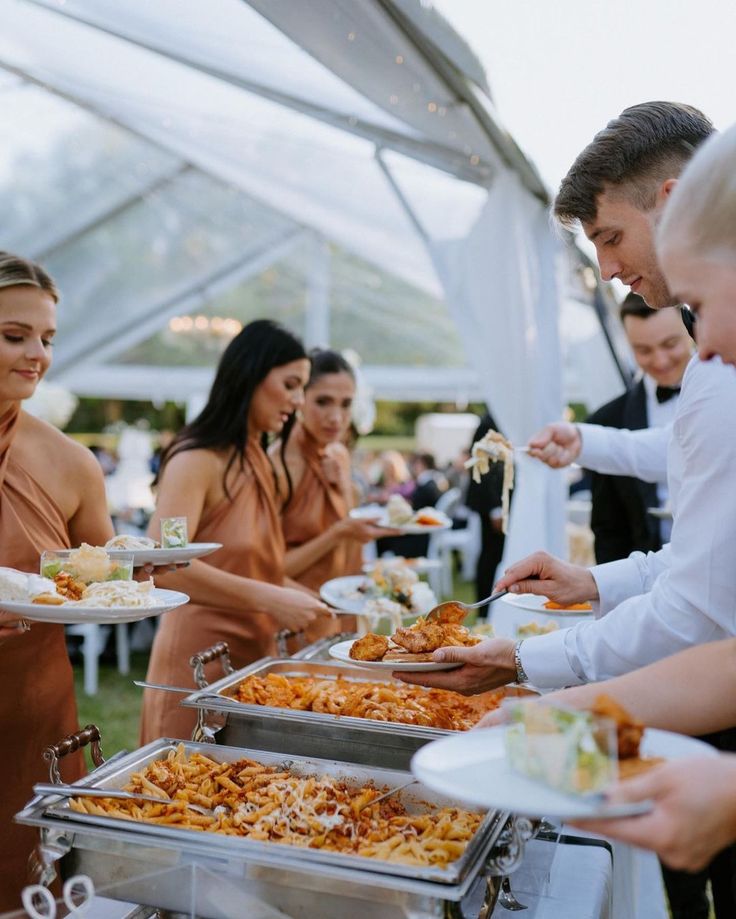 several people are serving themselves food from trays