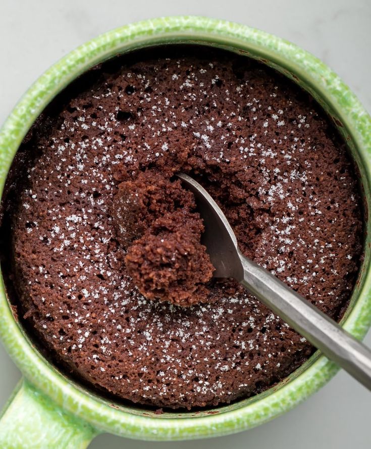 a spoon in a green mug filled with chocolate cake and sprinkled with powdered sugar