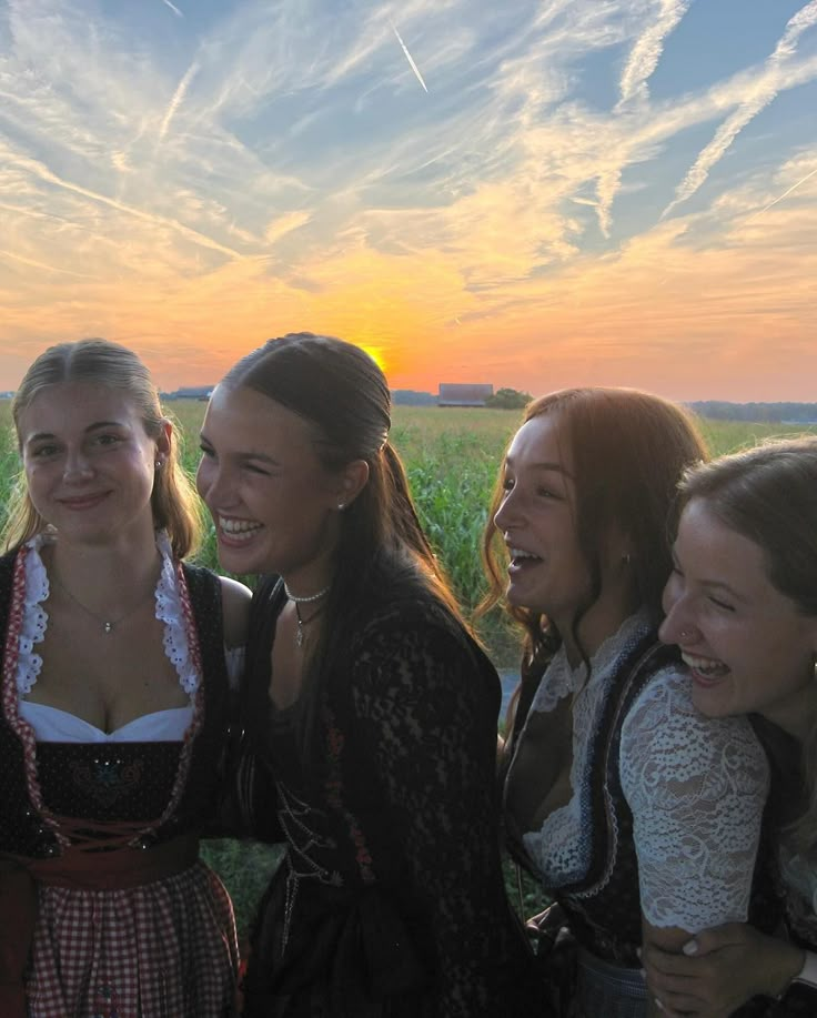 four young women are posing for the camera in front of a field with grass at sunset