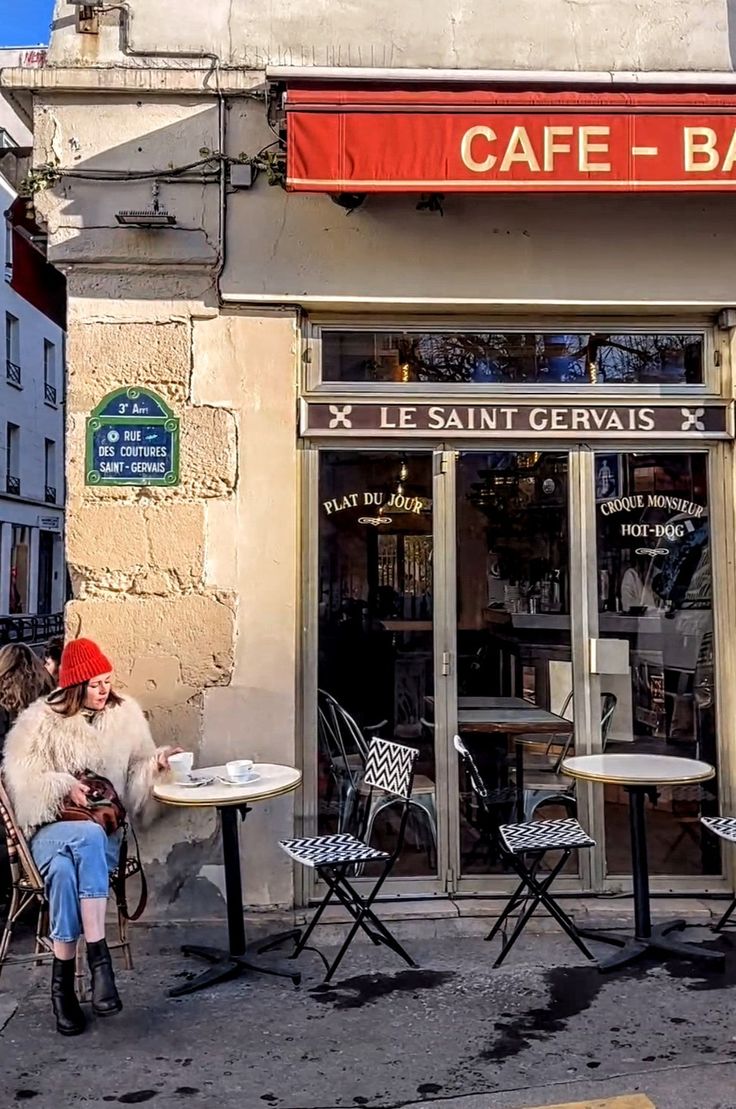 a woman sitting at a table in front of a cafe on the side of a street