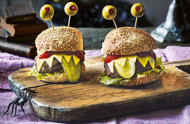 two cheeseburgers with pickles and tomatoes on a cutting board next to a spider