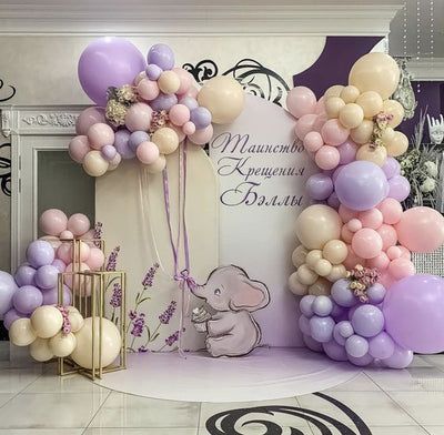 an elephant balloon arch is decorated with pastel pink, lavender and gold balloons for a baby's first birthday party