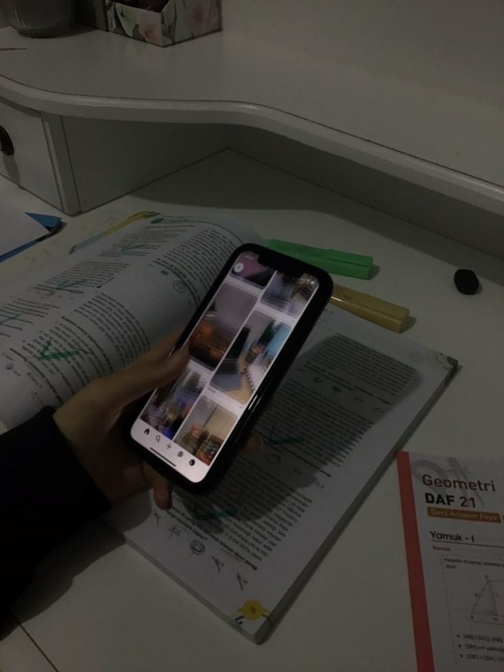 a person holding an iphone in their hand while sitting at a desk with papers and pens