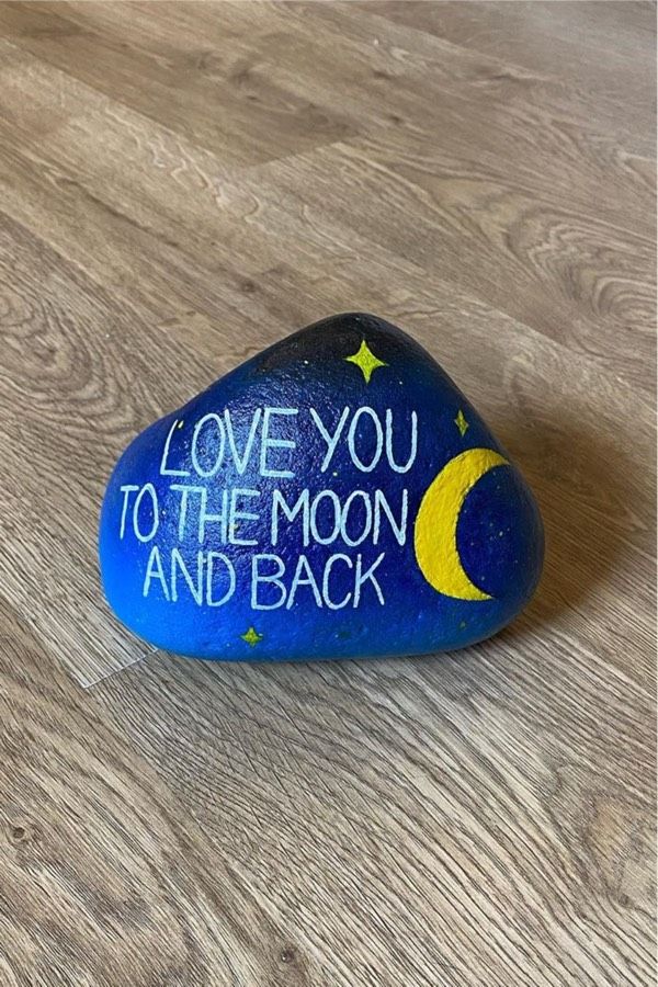 a rock with the words love you to the moon and back painted on it sitting on a wooden floor