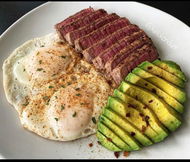 an egg, steak and avocado on a white plate with seasoning next to it