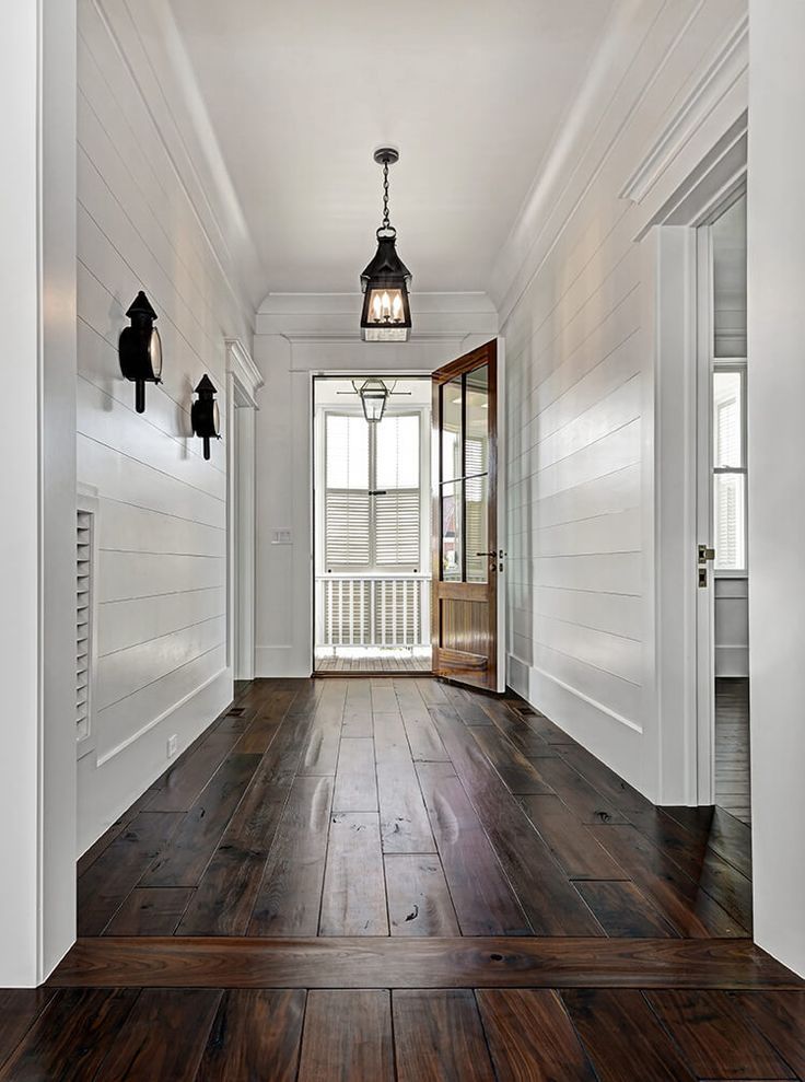 an empty hallway with wood flooring and white walls, along with two lanterns hanging from the ceiling