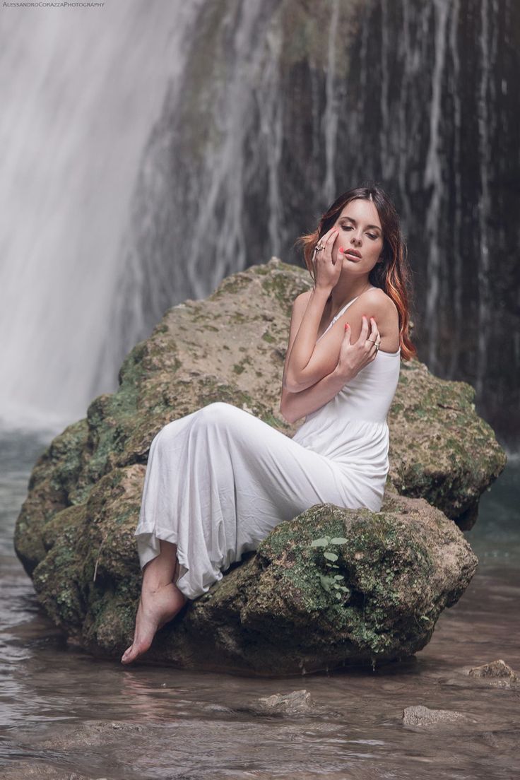 a woman sitting on top of a rock next to a waterfall