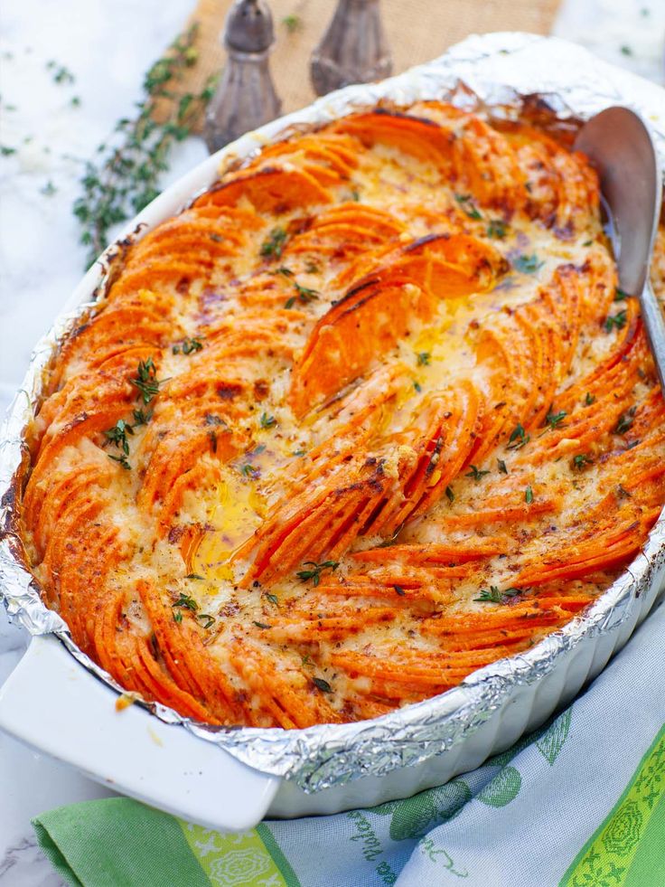 a baked dish with cheese and vegetables in it on a cloth next to utensils