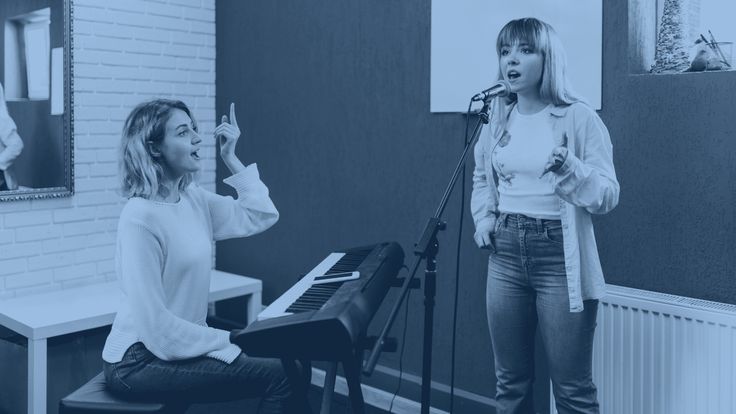 two women singing into microphones in front of a piano