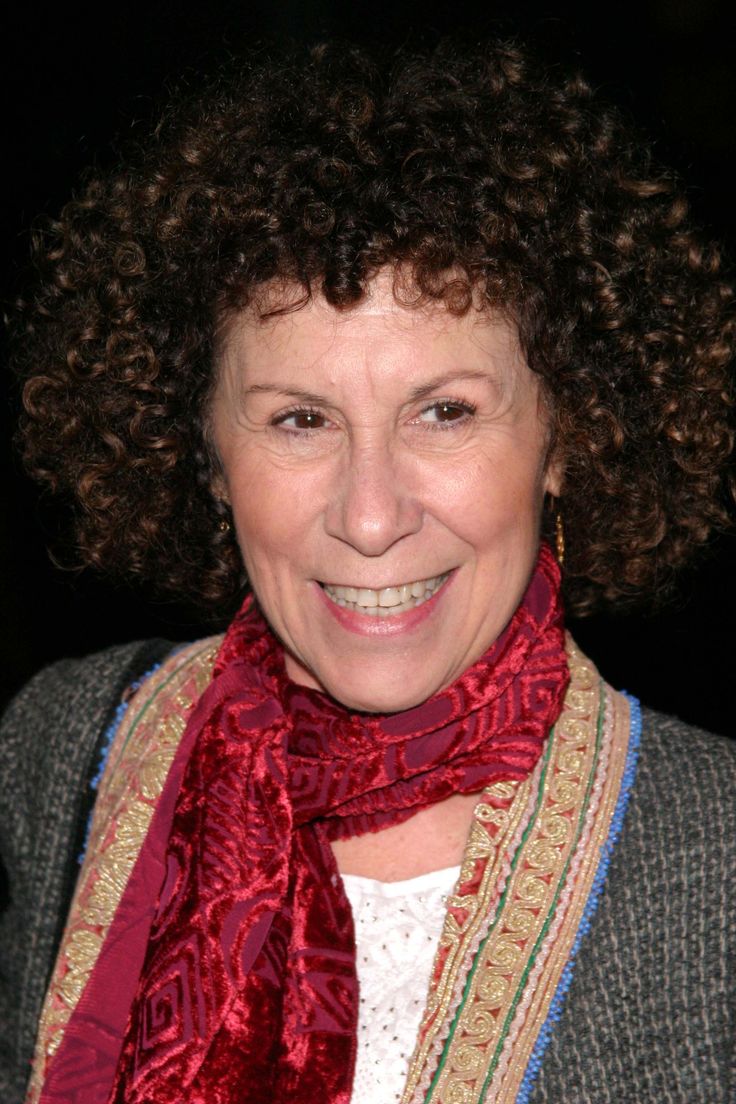 a woman with curly hair wearing a red scarf and smiling at the camera while standing in front of a dark background