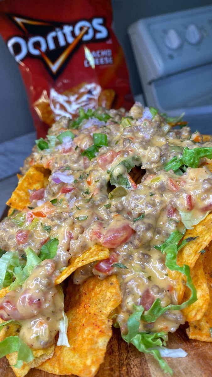 nachos with cheese, lettuce and tomato sauce on wooden cutting board