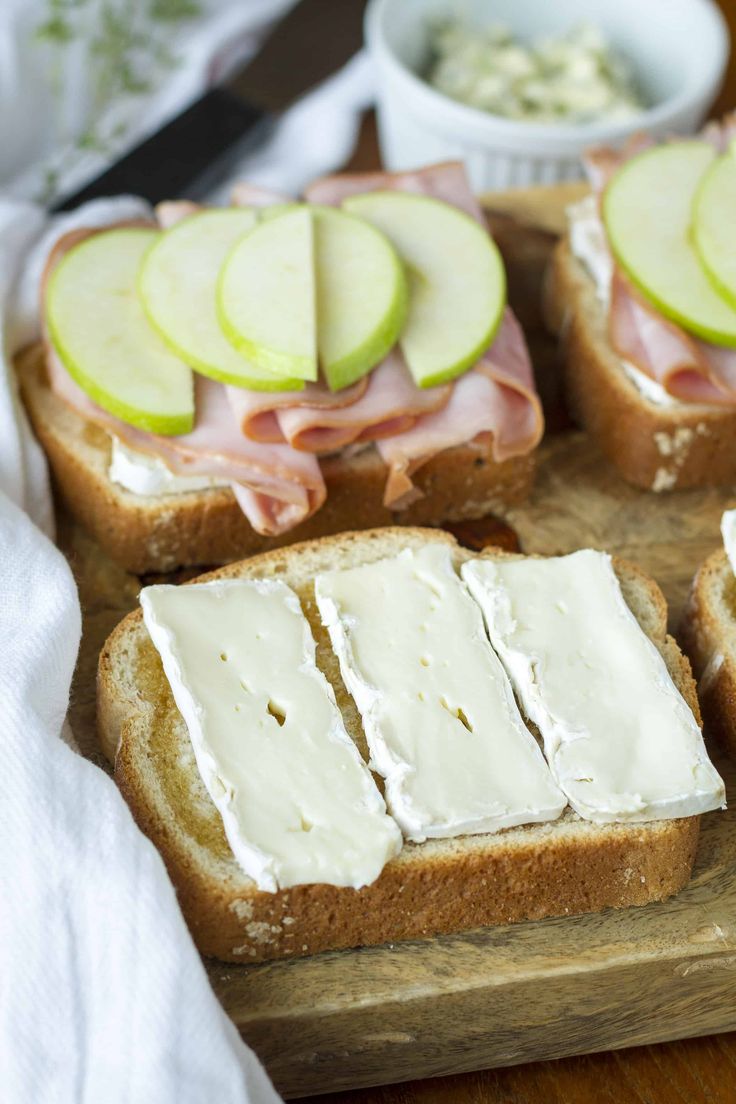 slices of bread with ham, cheese and apple slices on them sitting on a cutting board