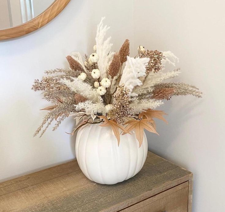 a white vase filled with flowers sitting on top of a wooden dresser next to a mirror