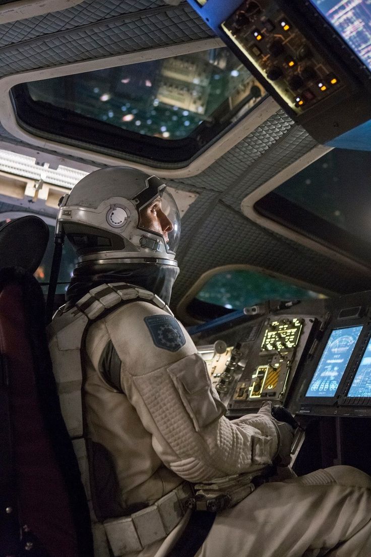 a man sitting in the cockpit of a space shuttle looking out at the city lights