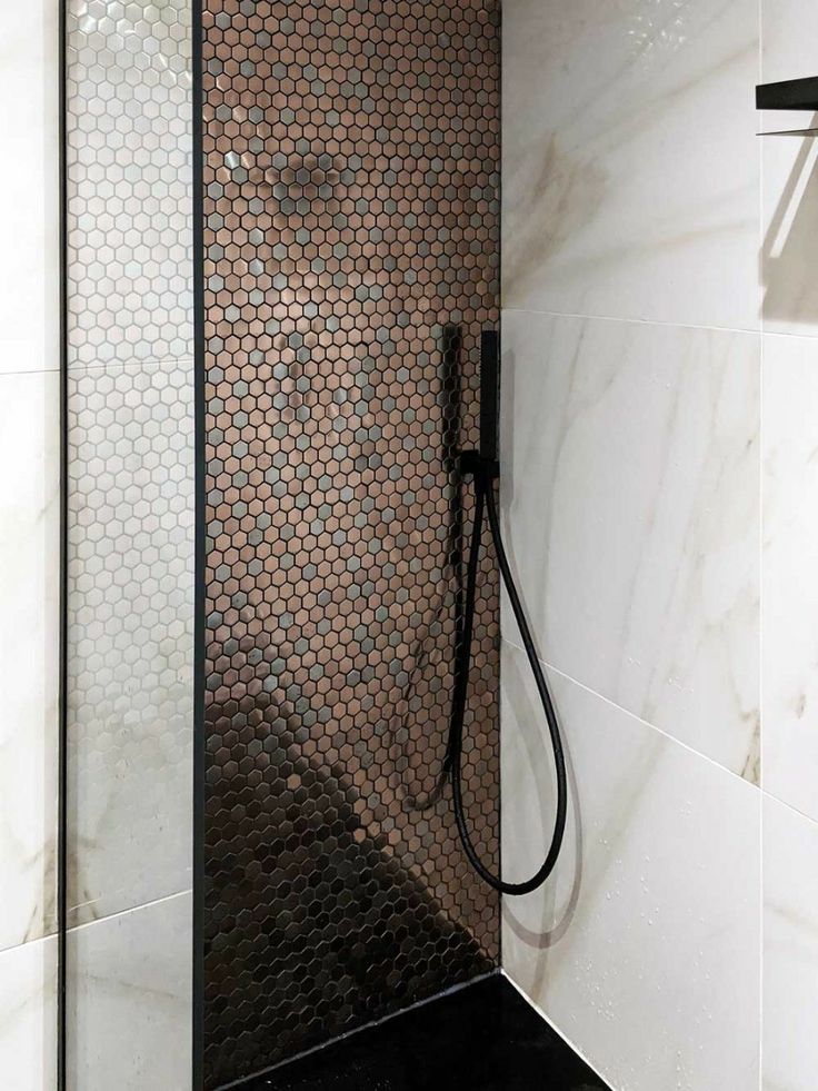 a shower head in the corner of a white tiled bathroom with black and brown accents