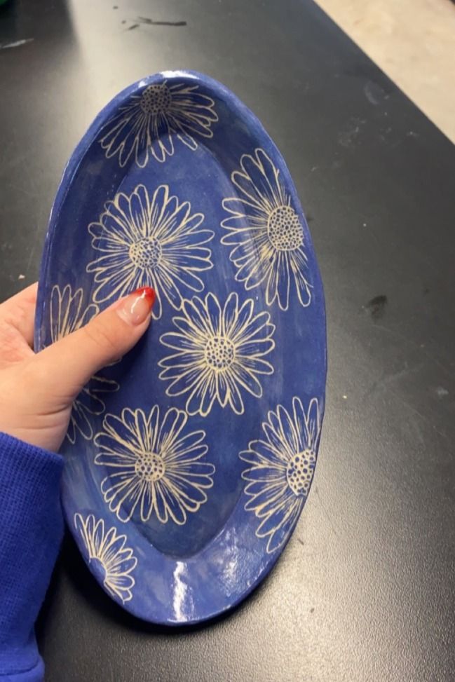 a blue plate with white flowers on it is held up by a woman's hand