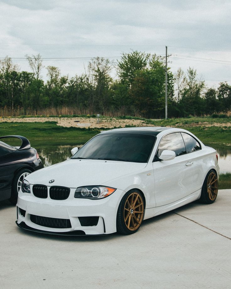 two cars parked next to each other in a parking lot with water and trees behind them