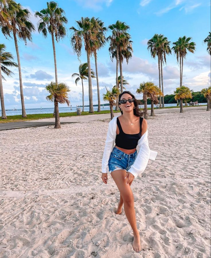 a woman standing on top of a sandy beach next to palm tree covered trees in the background