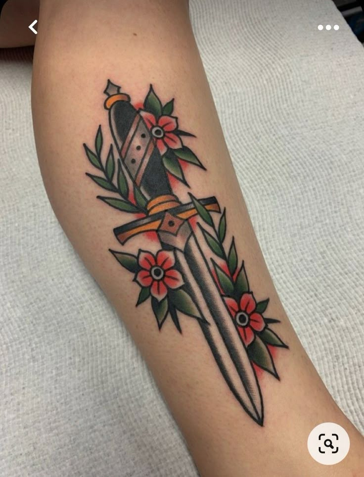 a tattoo on the leg of a woman with a knife and flowers around her arm