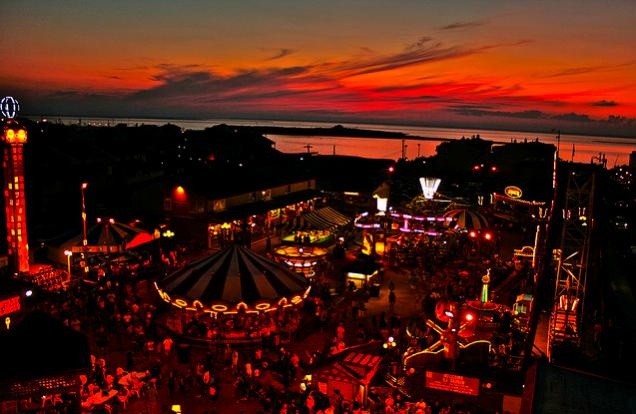 an aerial view of a fairground at night with the sun setting in the background