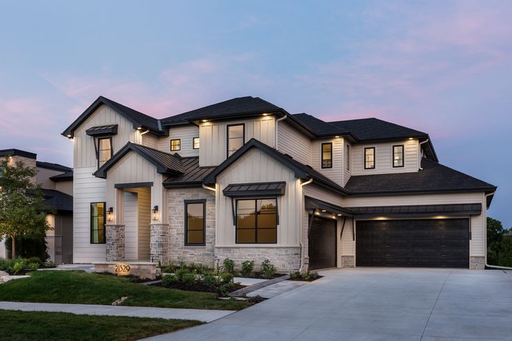 a two story house with lights on in the front yard and driveway leading to it