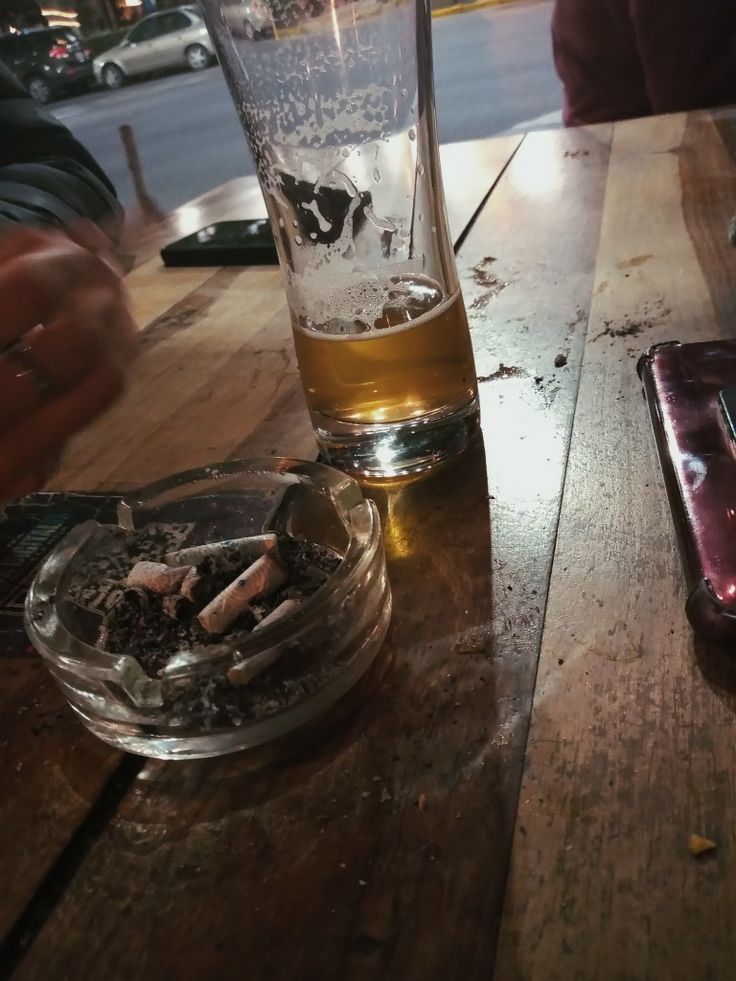 an empty glass sitting on top of a wooden table next to a cell phone and wallet