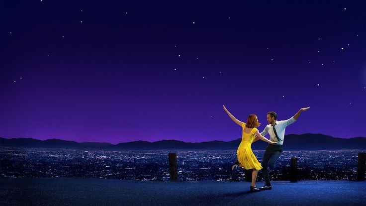 a man and woman dancing on top of a roof at night with the city lights in the background