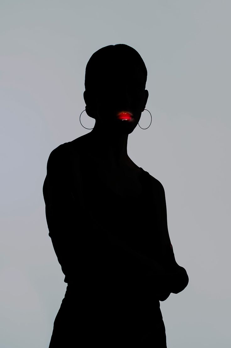 the silhouette of a woman with red light on her face is shown in front of a gray background