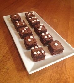 brownies with marshmallows are on a white plate sitting on a wooden table