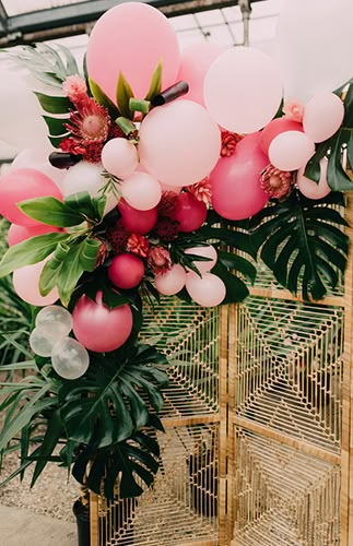 a bunch of balloons and greenery are hanging from the ceiling in front of a cage