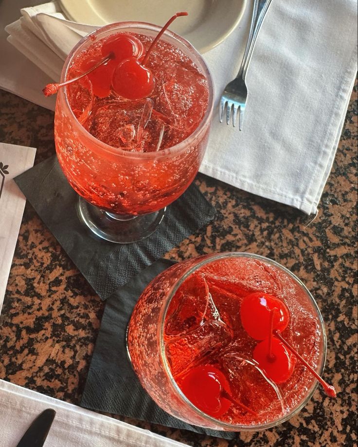 two glasses filled with red liquid on top of a table next to silverware and napkins