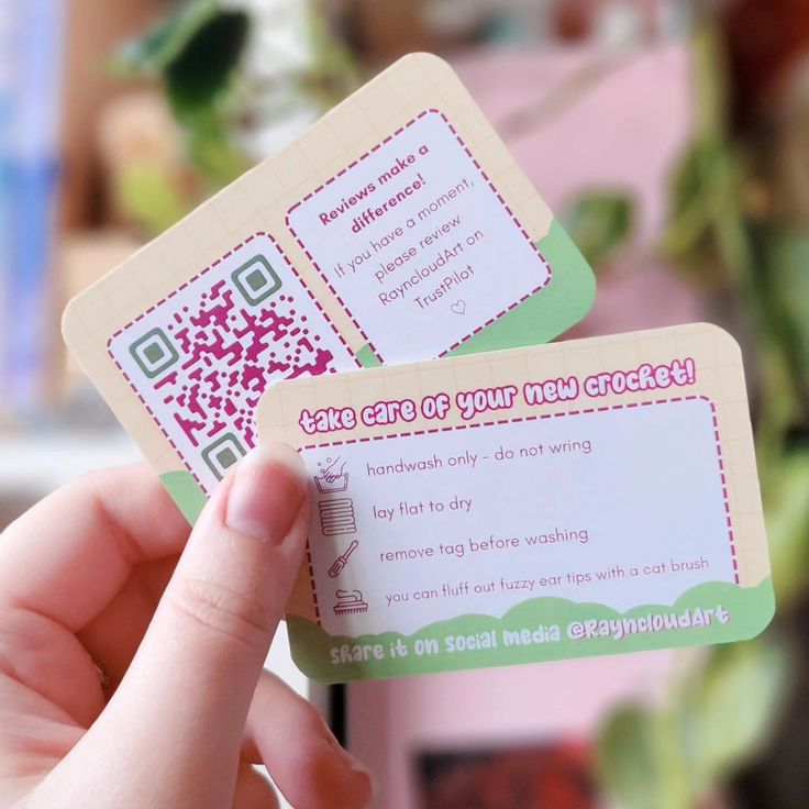 someone holding up two business cards with qr code printed on them in front of a potted plant